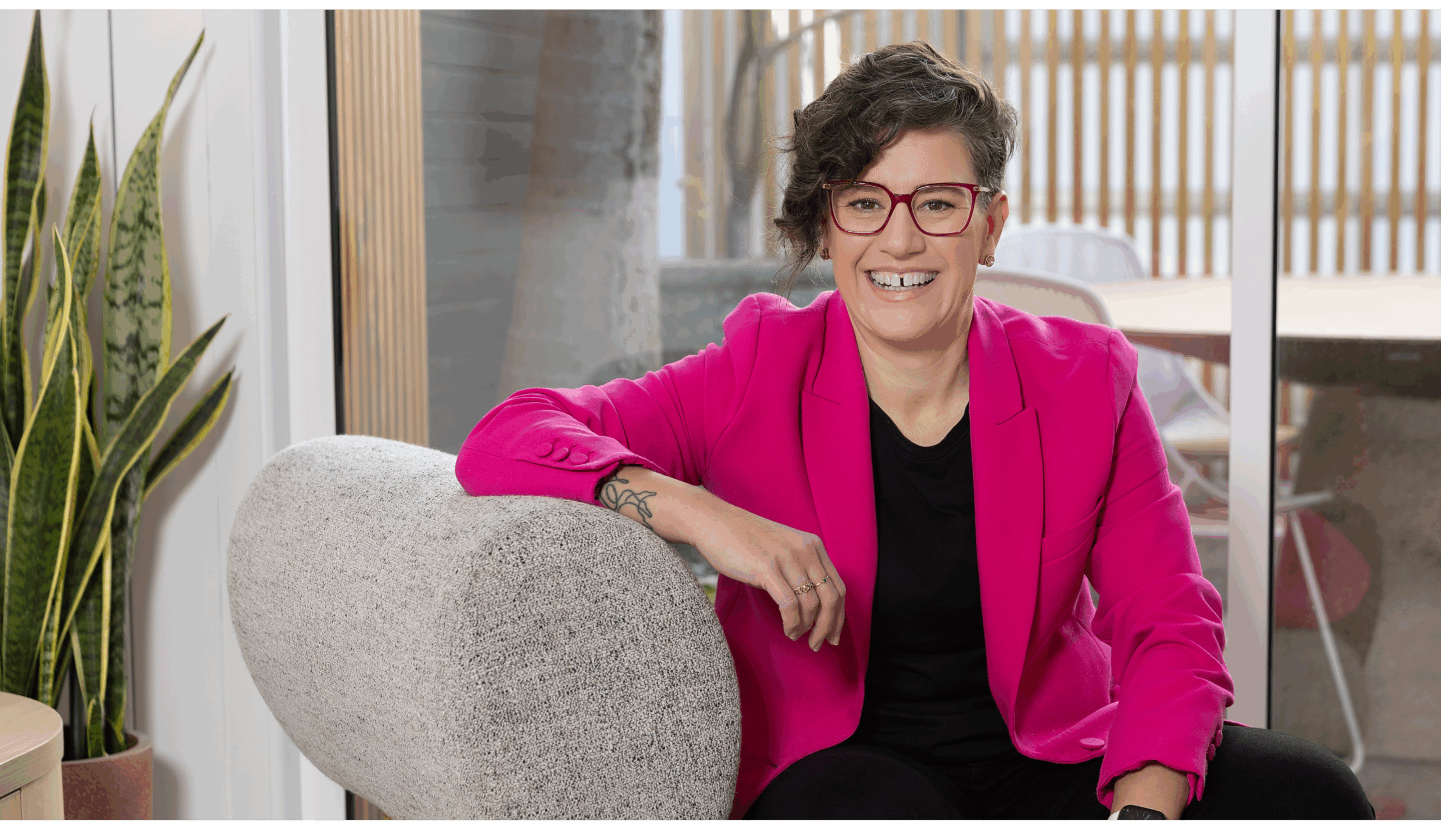 Hannah is sitting on a grey couch, smiling at the camera. She's wearing a bright pink jacket.